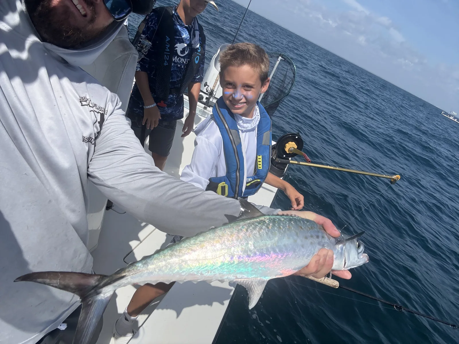 An adult holds a silvery fish while a camper smiles on the boat.
