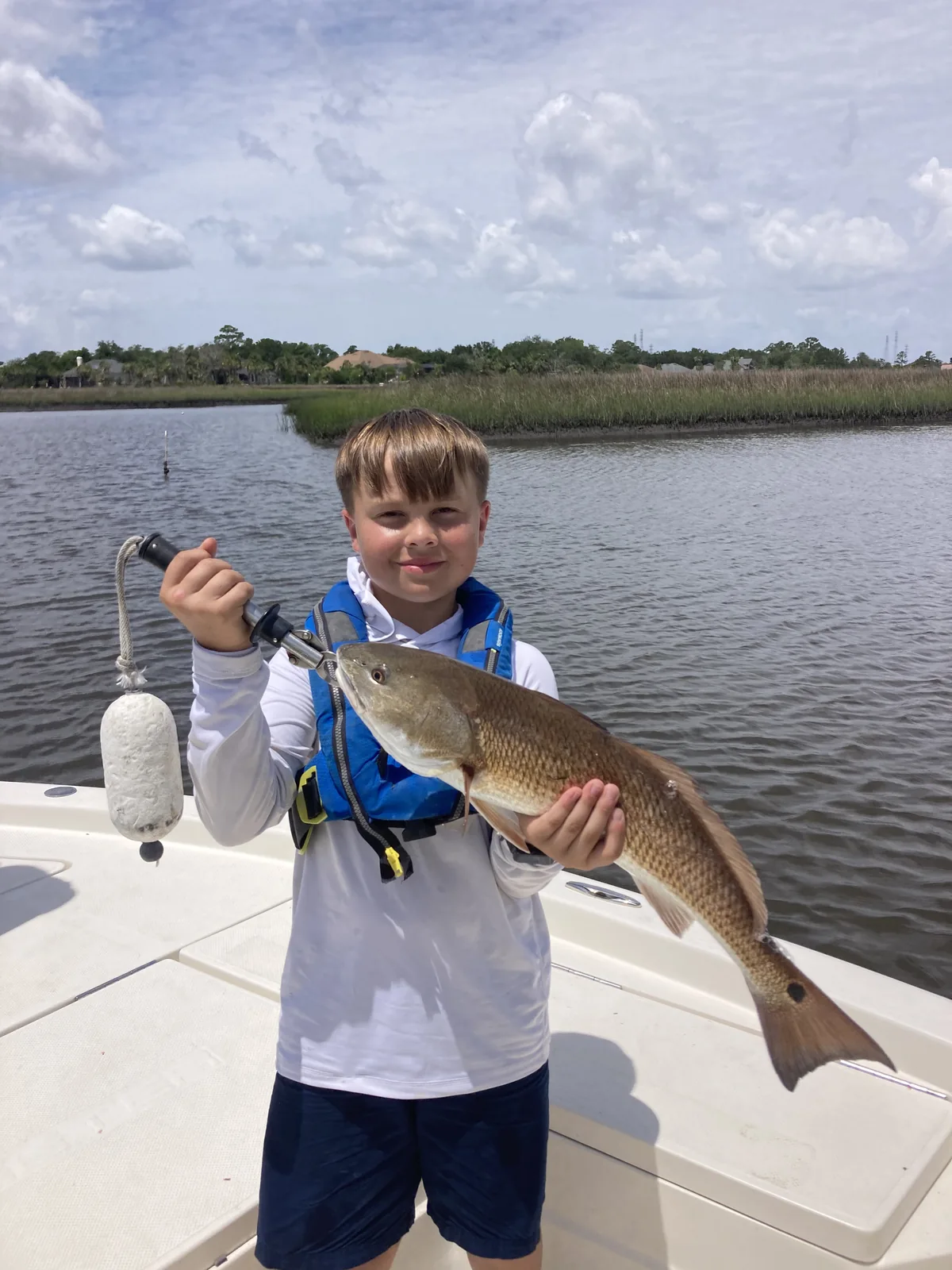 A camper displays a catch from a boat beside a grassy shoreline.
