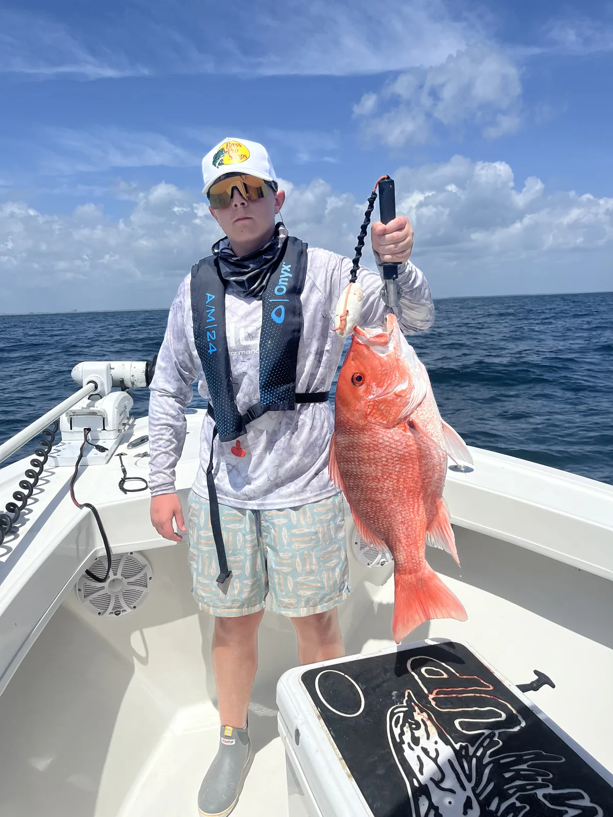A camper displays a large red fish while standing aboard a boat.