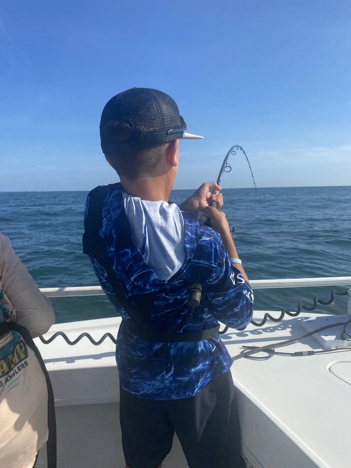 A young angler reels in with a bent rod aboard a boat.