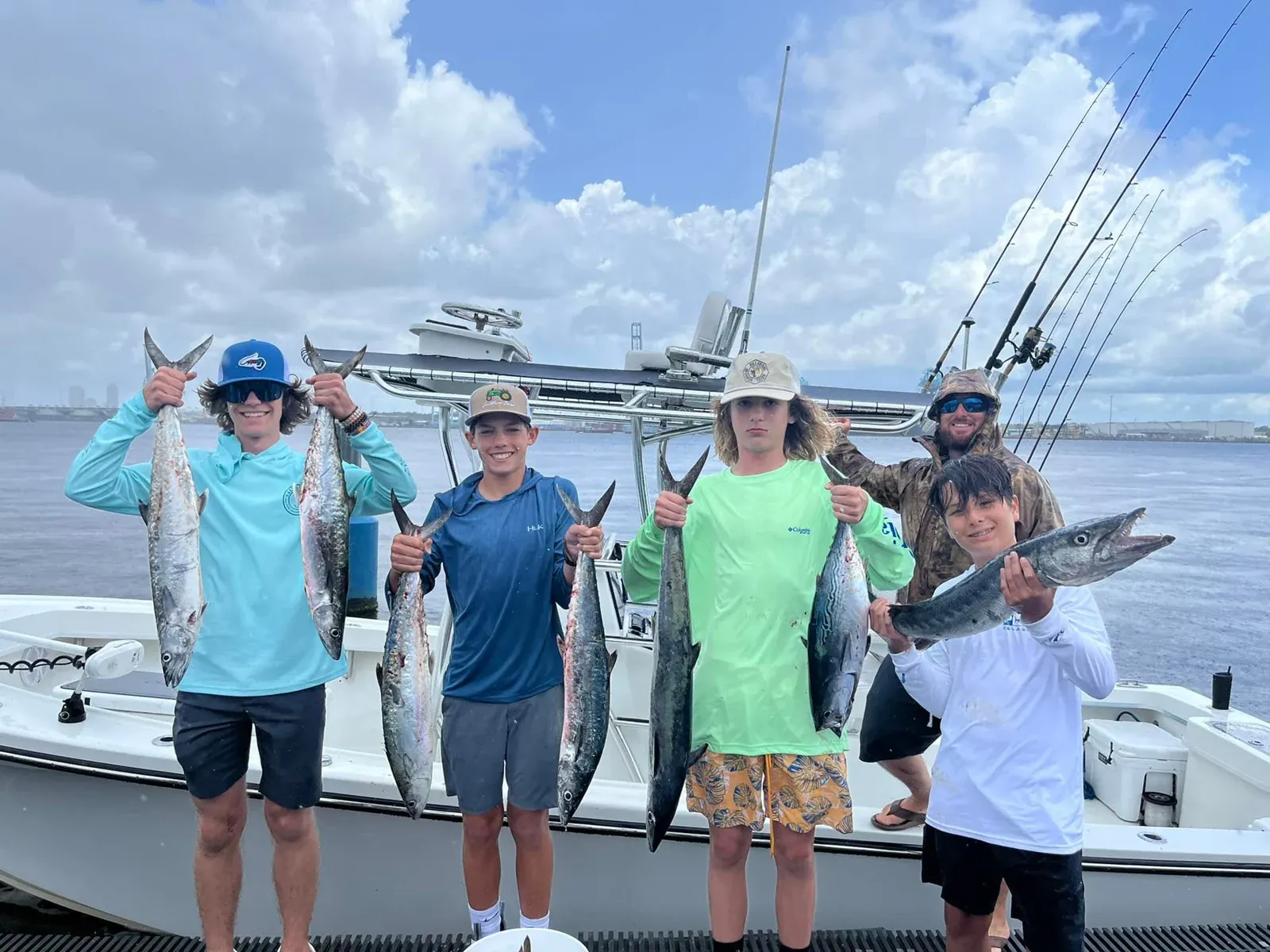 Young anglers and a captain display kingfish beside their charter boat.