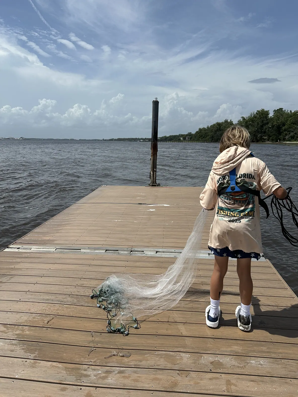A camper prepares a cast net on a wooden dock.
