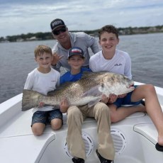 Capt. Travis Wilson with three campers and a big black drum