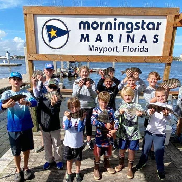 A big group of campers and counselors holding their catch at the marina