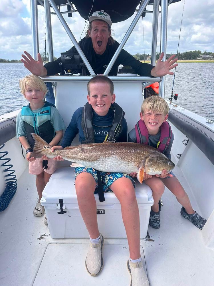 Three day campers and their captain holding a bull redfish on the boat