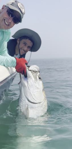 Captain and camper lifting a tarpon at the side of the boat