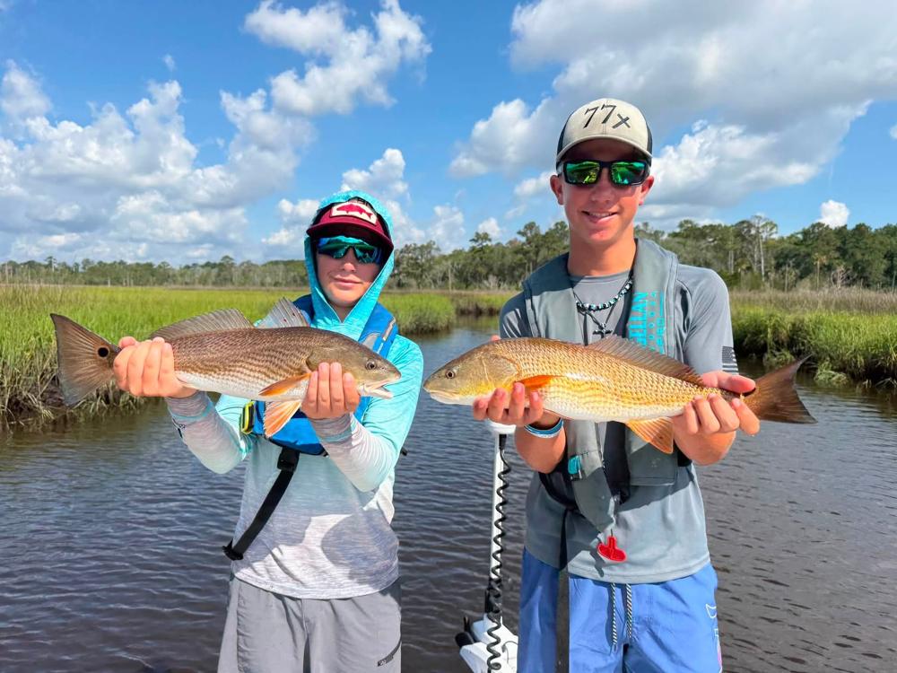Two Overnight Camp campers holding redfish in the St. Johns River marsh