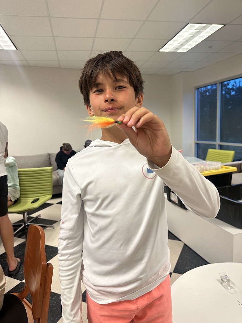 Overnight camper holding a fly he tied in the dorm lounge